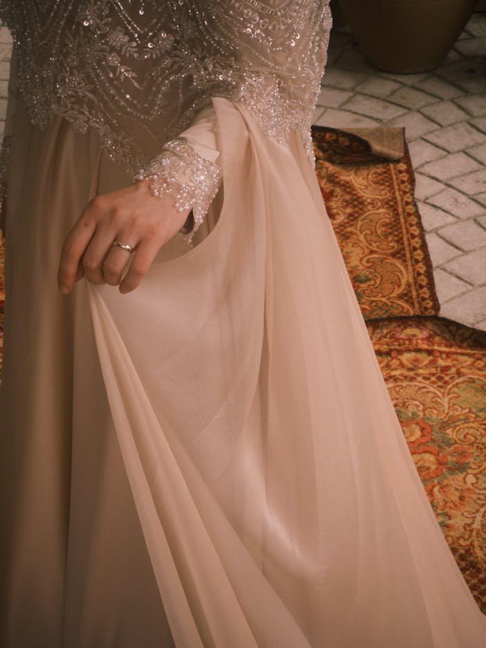 Close-up of an elegant bridal gown with intricate beading and lace details on a vintage carpet.